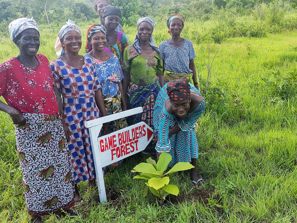 Aufforstungsprojekt Boardgame Road: Ghanaerinnen vor dem Schild des Game Builders Forest